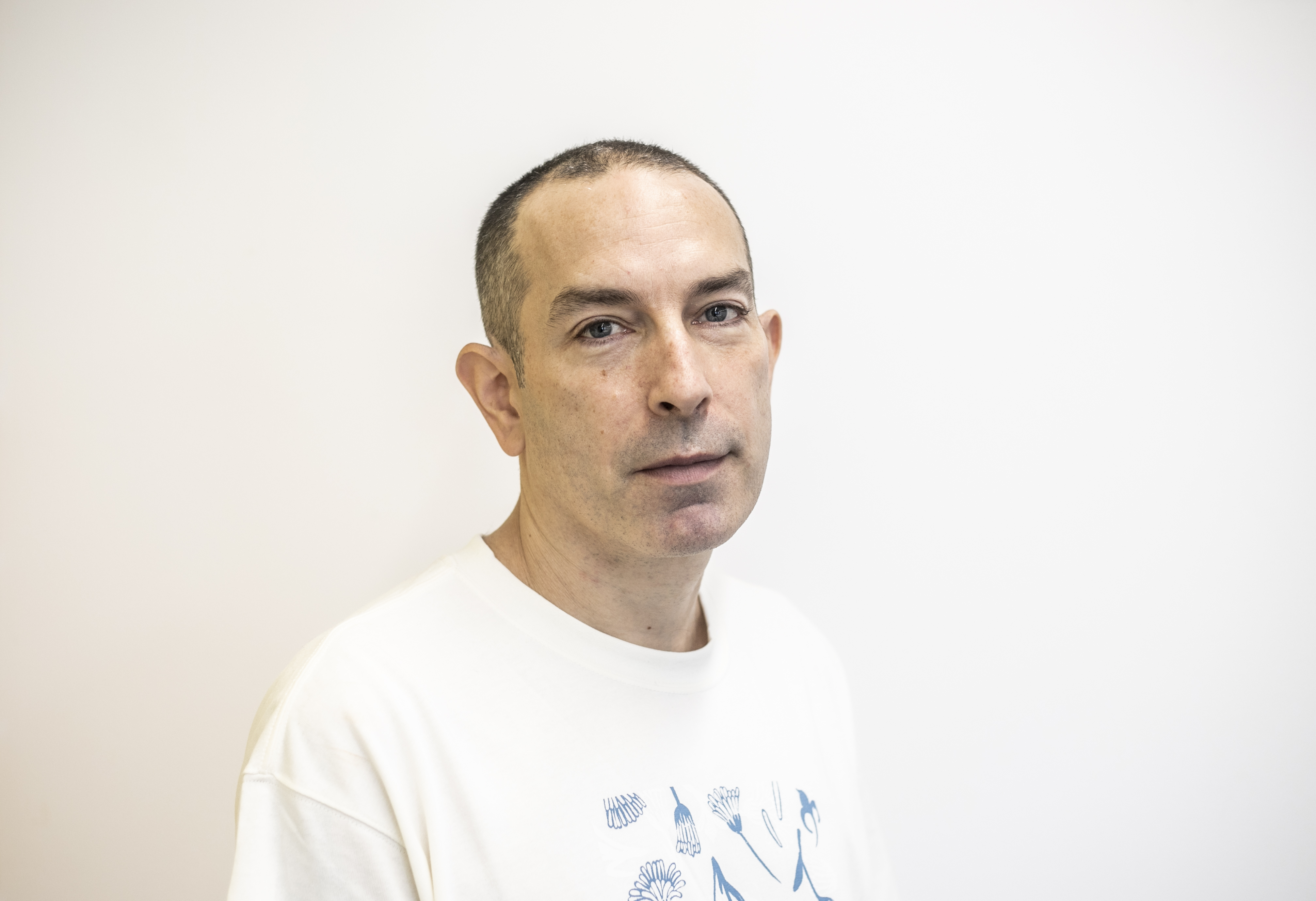 Headshot of Barny Darnell. White male with shaved head and white t-shirt with white background